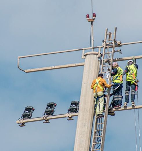 Scaling - Workers performing maintenance on a high mast lighting structure against a clear sky.