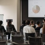 Market Share - Business professionals attending a seminar with a presentation on market share, highlighting diverse participation.