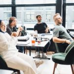 Product Diversification - Modern office setting with diverse team in discussion, seated around a table by large windows.