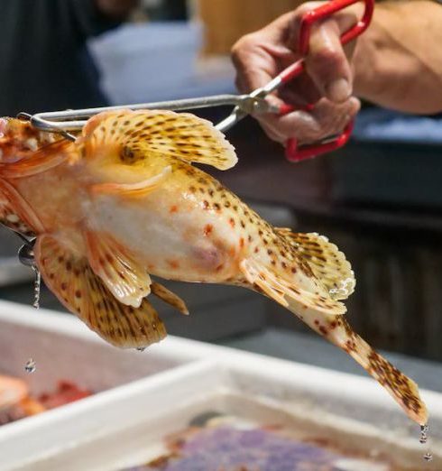 Market Demand - A vendor holds a fresh fish with tongs at a bustling seafood market.