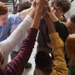 Company Culture - A diverse group of professionals high-fiving in a modern office, showcasing teamwork and collaboration.