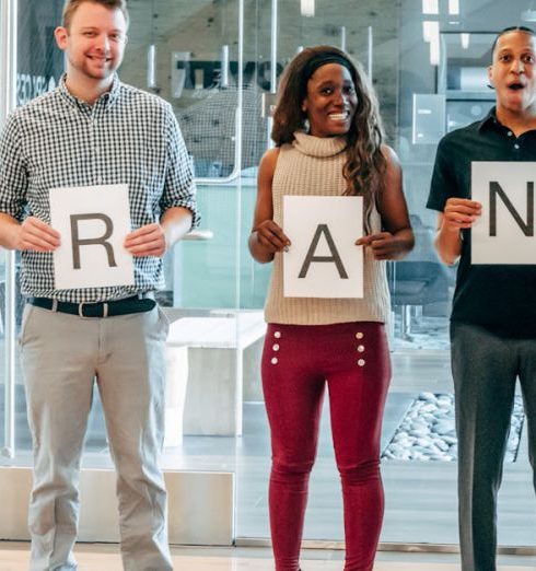 Brand Community - Diverse business team smiling and holding signs spelling 'BRAND' in a modern office.