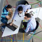 Networking - Three men collaborating over a laptop in a modern, geometric-themed office space.