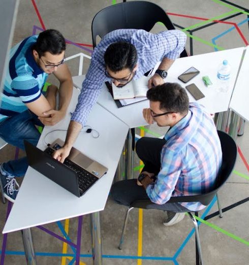 Networking - Three men collaborating over a laptop in a modern, geometric-themed office space.