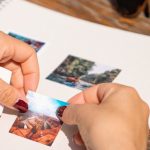 Personalization - Hands arranging photos in a scrapbook under sunlight, capturing summer memories.