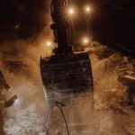 Difficult Customers - Emergency workers conduct a night rescue in debris after a disaster, illuminated by harsh lights.