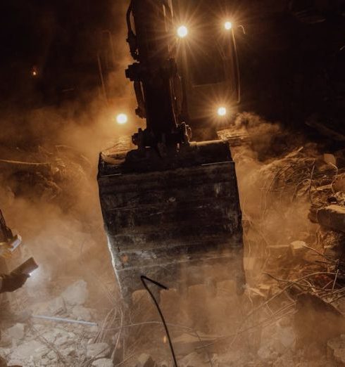 Difficult Customers - Emergency workers conduct a night rescue in debris after a disaster, illuminated by harsh lights.