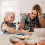 Happy young girl with her mother making dough